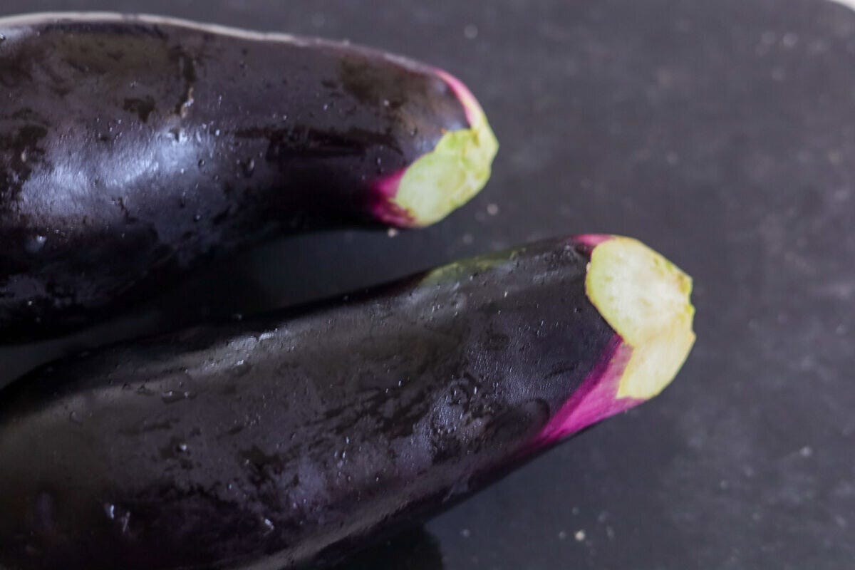 黒いまな板に置かれた2本の黒紫色のなす