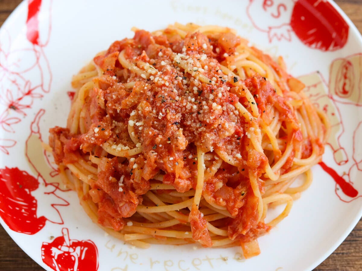 トマト柄の白い皿にツナトマトパスタを盛り粉チーズと黒こしょうをかけた完成品の俯瞰写真