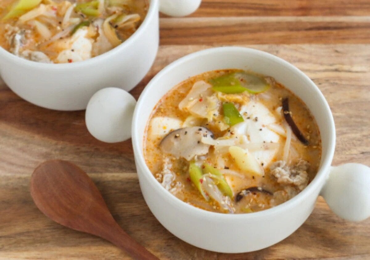 白いカップに盛った豆腐ともやしの豚キムチ豆乳スープ 白いスープカップに入った赤みのある豚キムチ豆乳スープ。豆腐・しいたけ・もやし・長ねぎが入り黒こしょうがふられている