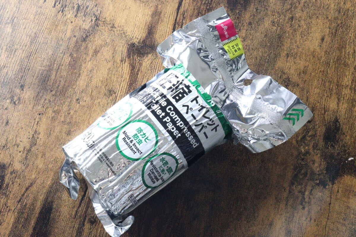 開封途中のアルミ包装に入ったダイソーの備蓄用圧縮トイレットペーパーが木目のテーブルに置かれている。