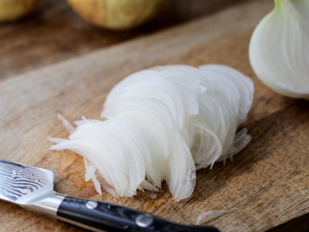 木のまな板の上で繊維に沿って薄くスライスした新玉ねぎ 木のまな板の上で繊維に沿って薄くスライスした新玉ねぎ