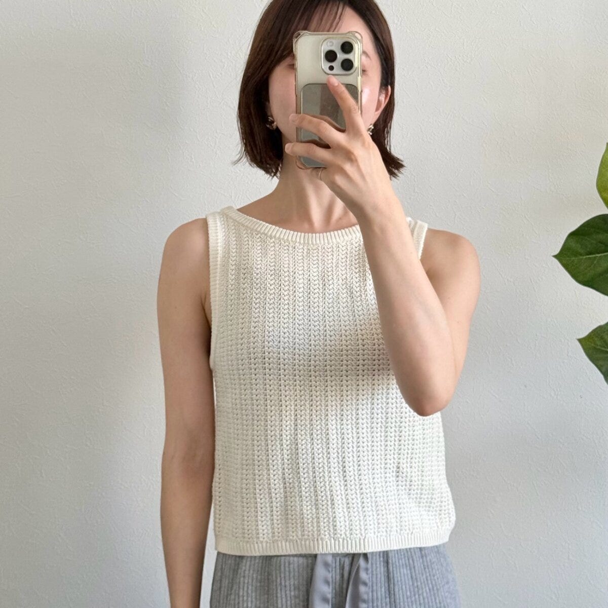白いニットタンクトップを着た女性がスマホで顔を隠している 白いニットタンクトップを着た女性がスマホで顔を隠している