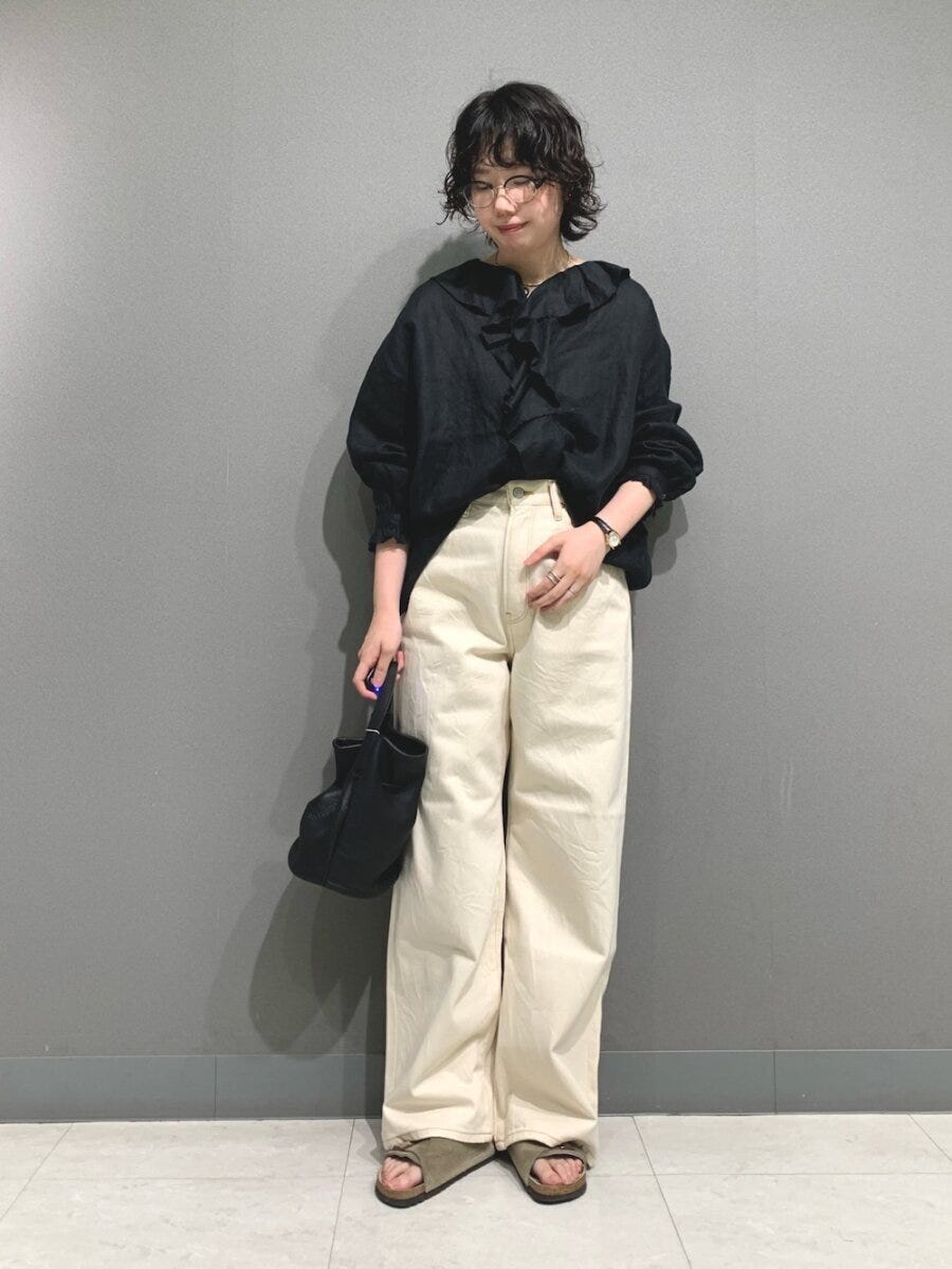 黒のフリルブラウスとアイボリーワイドパンツの女性