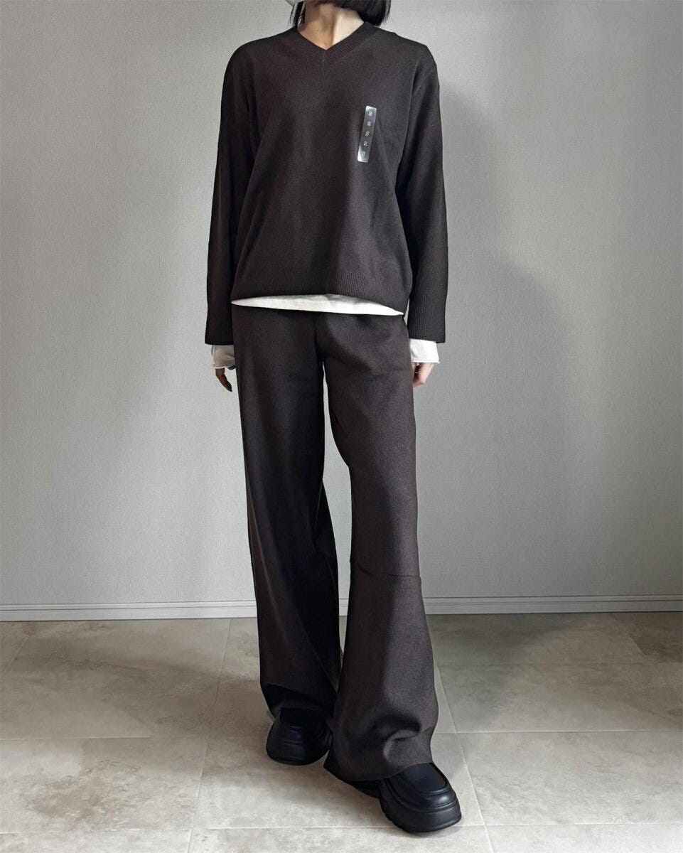 ダークブラウンのニットパンツに同色のVネックニットと白Tシャツを合わせたセットアップ風コーデの女性