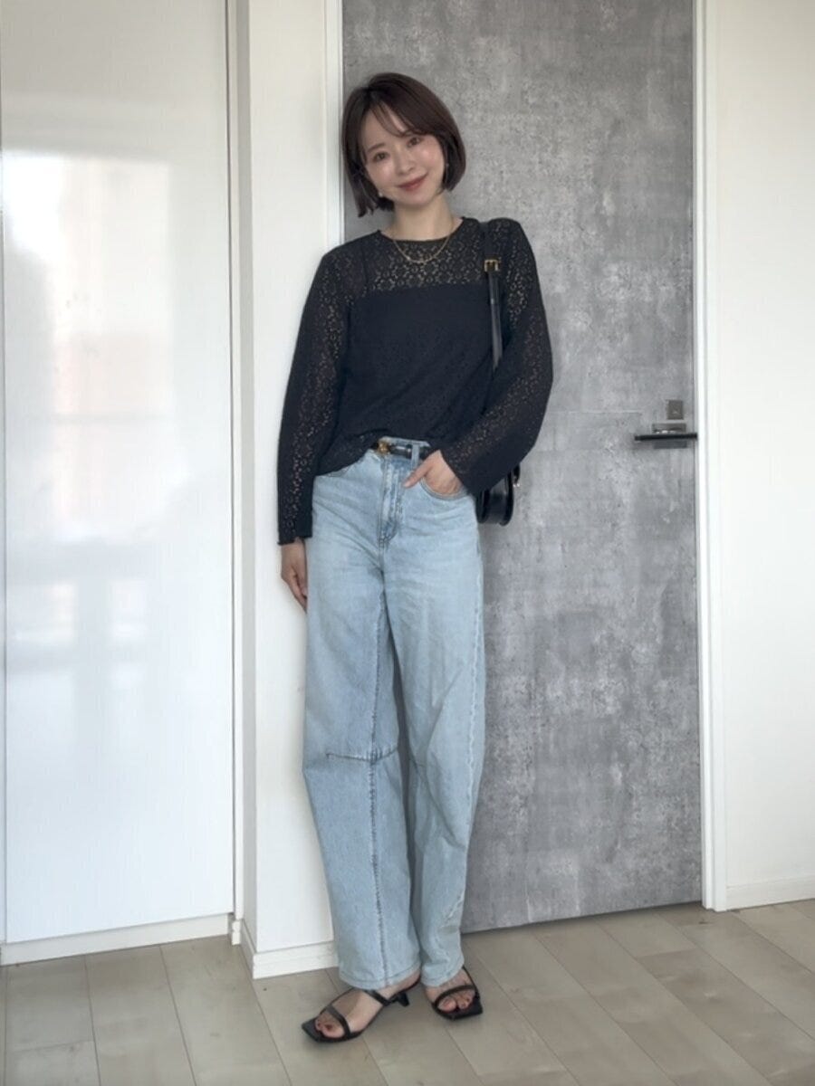 黒いレースブラウスとデニムのパンツスタイルで立つ女性