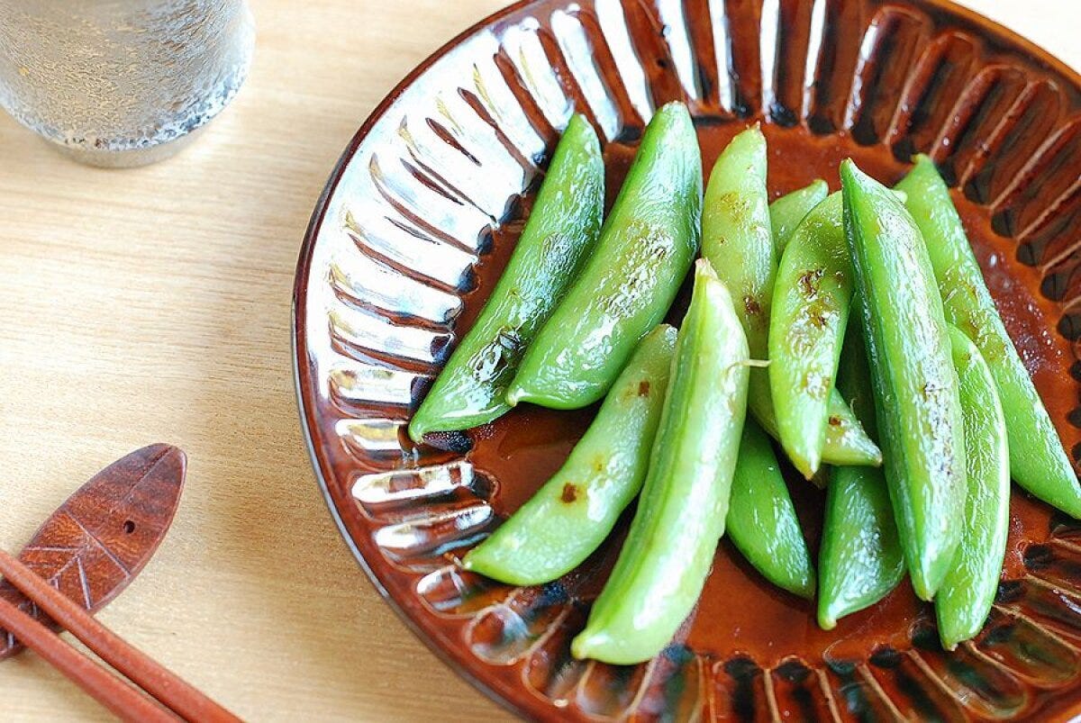 茶色の和食器に盛られたスナップエンドウのバター醤油炒め、奥にグラスを置いた完成写真