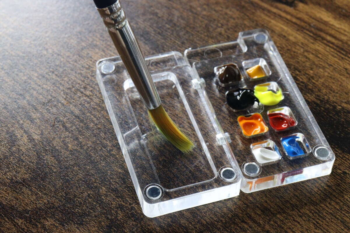 絵の具が入れられた透明なパレットと、その隣に置かれた絵筆