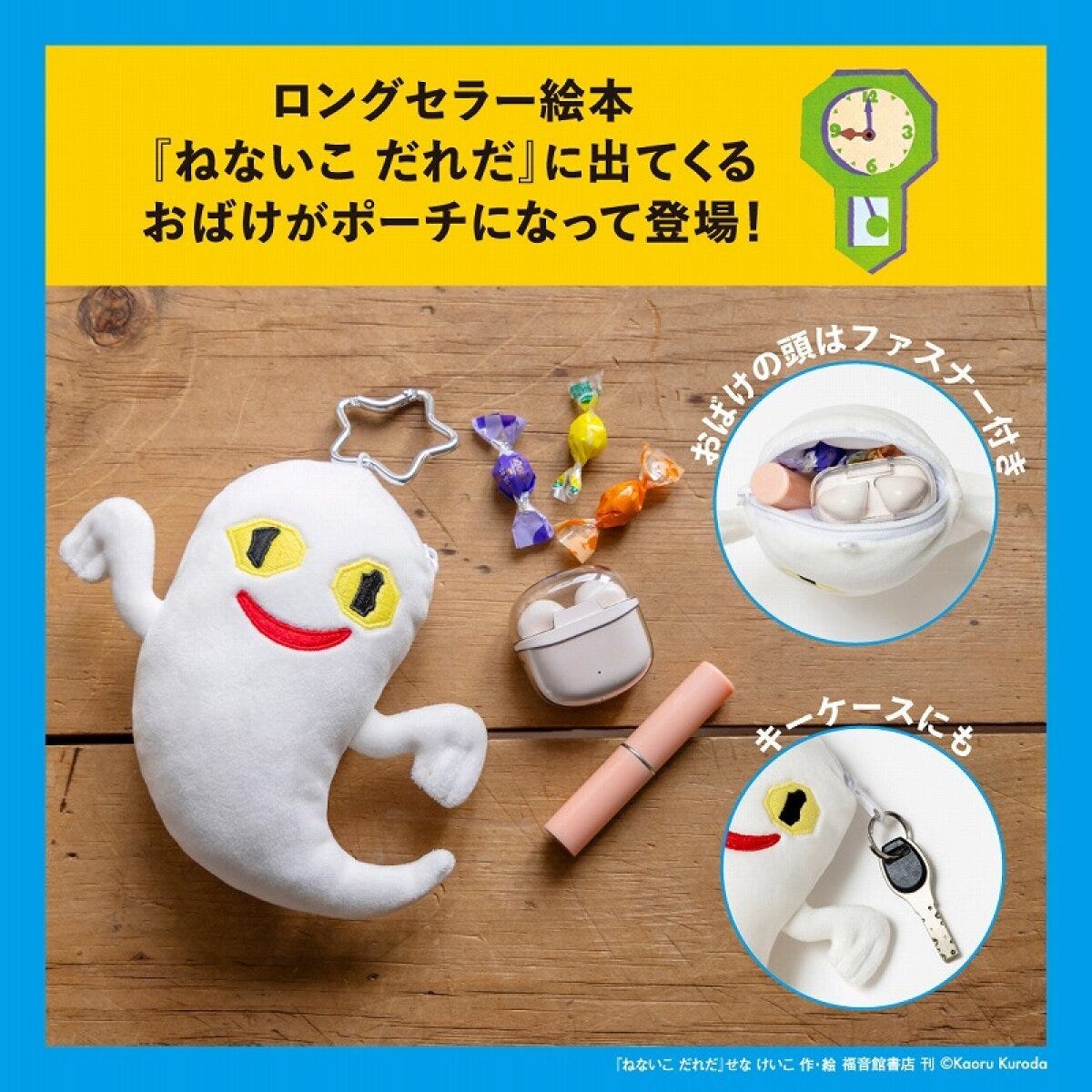 ねないこ 木目の床の上で、星形カラビナを付けた黄色い目と赤い口の白いおばけぬいぐるみポーチが横たわり、隣に包み紙キャンディとAirPodsケース、ピンクのリップが並ぶ俯瞰写真