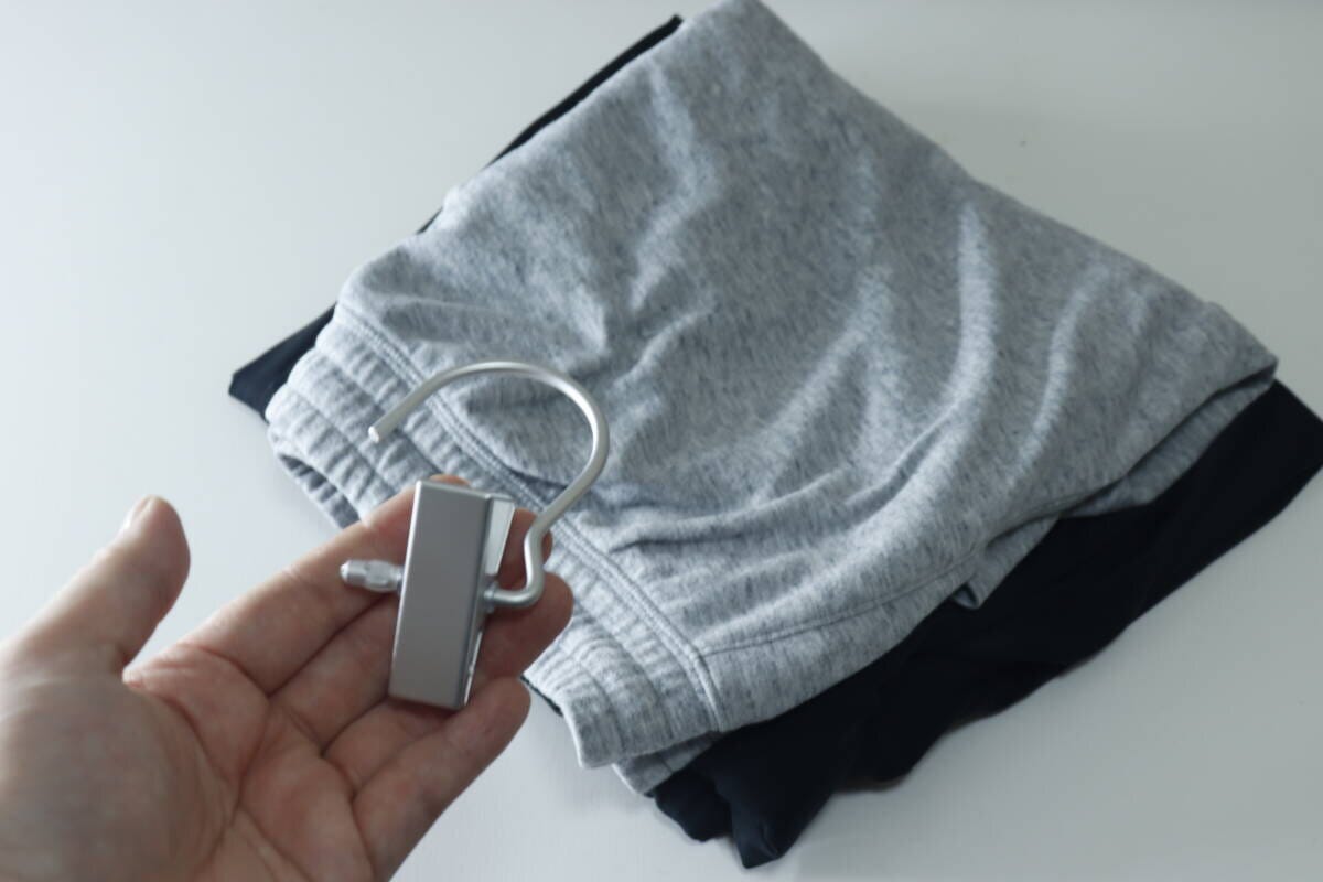 手に持ったアルミフックピンチと、畳まれたスウェットパンツが白いテーブルに置かれている