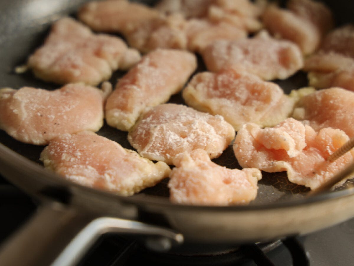 フライパンに油をひき、片栗粉をまぶした鶏むね肉のそぎ切りを並べて焼いている様子 フライパンに油をひき、片栗粉をまぶした鶏むね肉のそぎ切りを並べて焼いている様子