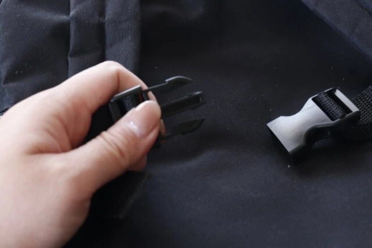 女性の指が黒いリュックの肩紐に取り付けられた肩ズレ防止ベルトのバックルを外そうとしている 女性の指が黒いリュックの肩紐に取り付けられた肩ズレ防止ベルトのバックルを外そうとしている