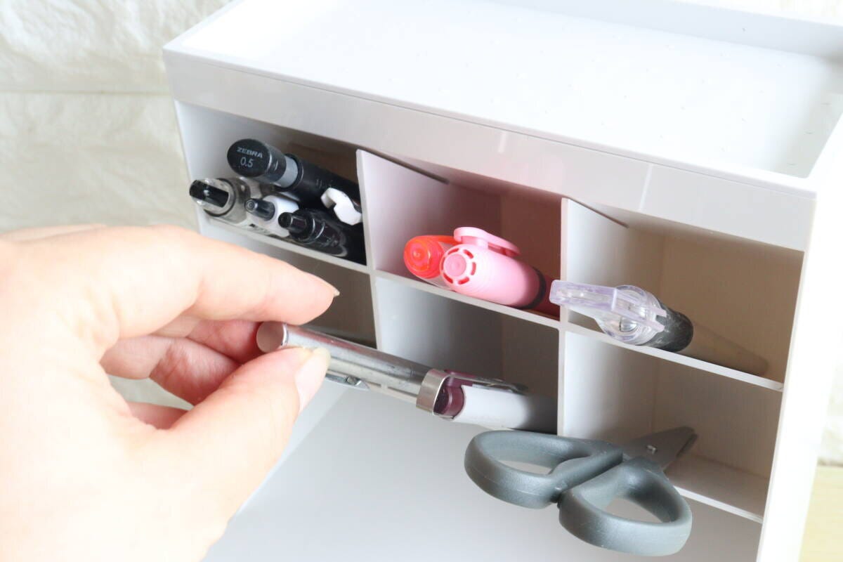白い収納ケースの仕切りにペンやハサミを収納する女性の手元