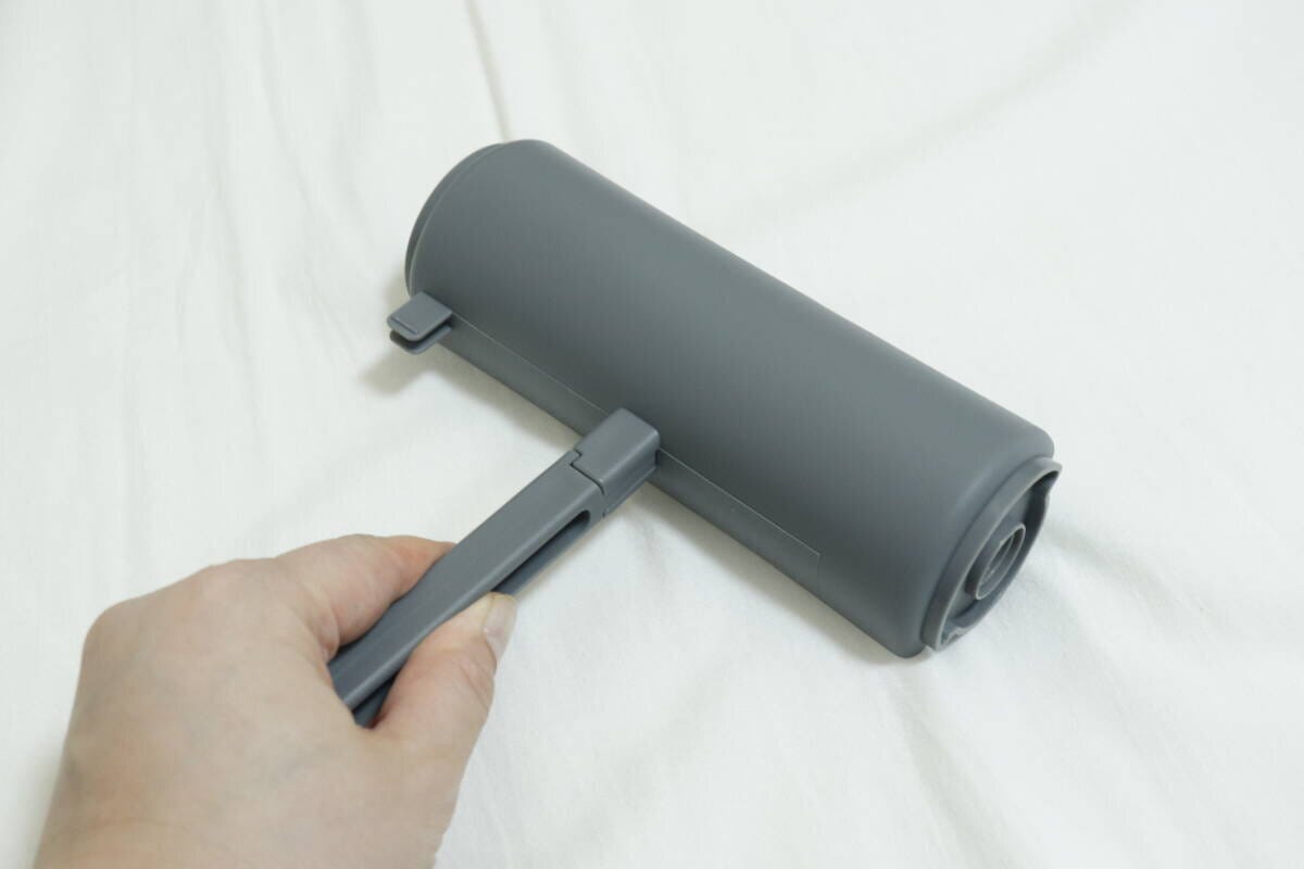 粘着テープをセットしたカーペットローラーで床を掃除する手 粘着テープをセットしたカーペットローラーで床を掃除する手