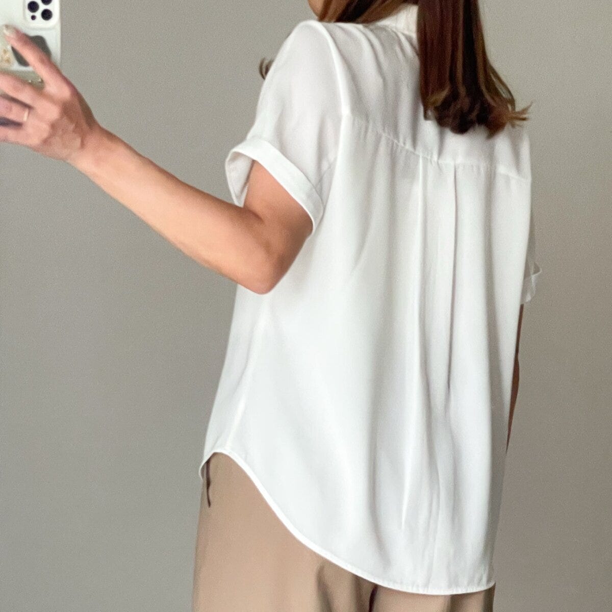 白い半袖シャツとベージュパンツの女性の後ろ姿がスマホで自撮り 白い半袖シャツとベージュパンツの女性の後ろ姿がスマホで自撮り