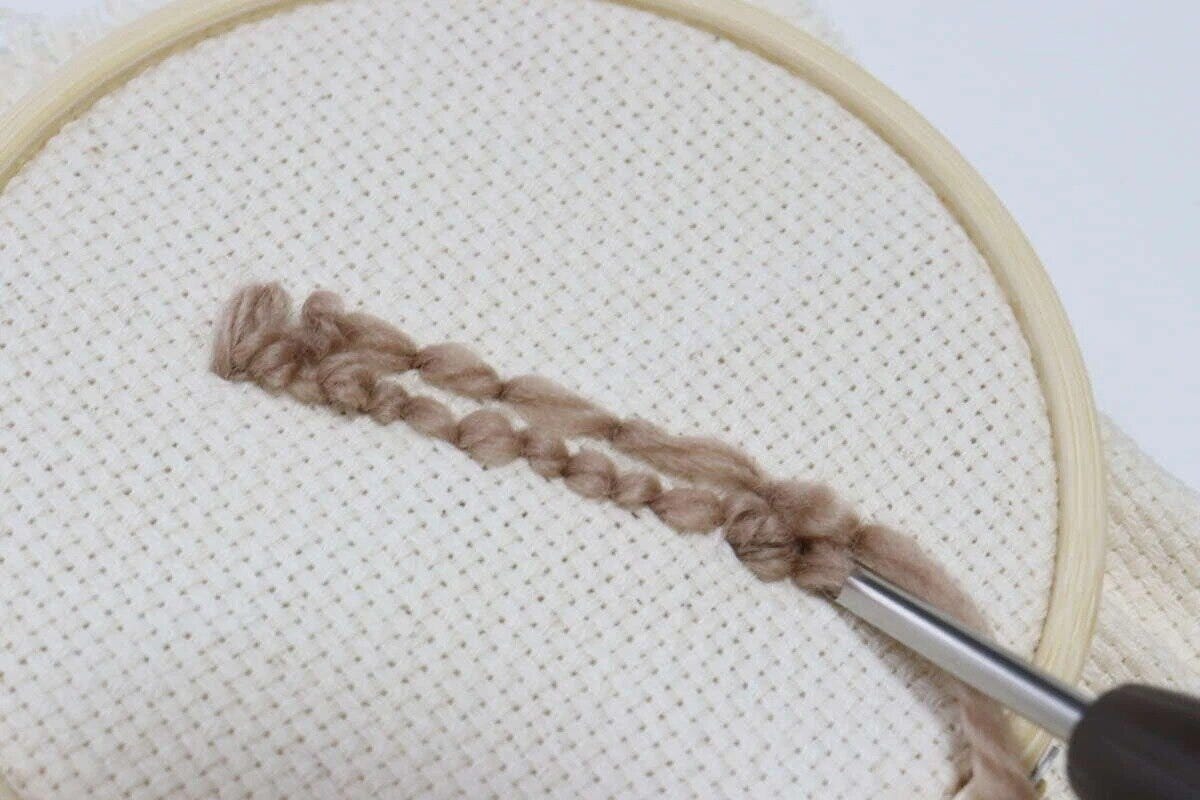 刺繍枠に張られた布にパンチニードルで茶色い毛糸を刺している様子 刺繍枠に張られた布にパンチニードルで茶色い毛糸を刺している様子