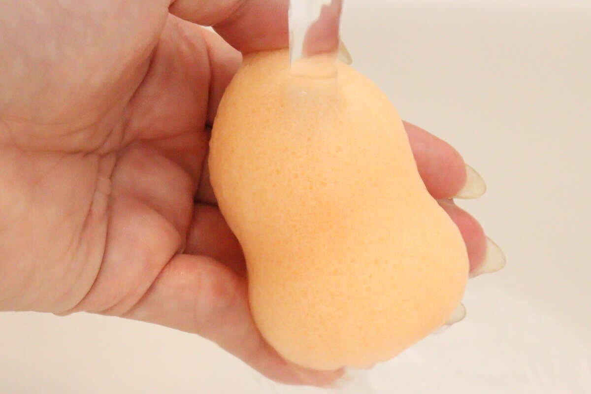 蛇口から流れる水でひょうたん型の洗顔パフを濡らしている手元