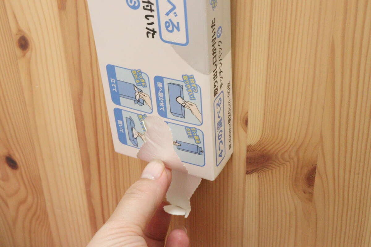 木目調の壁に吊るしたパッケージからキッチンパックを一枚引き出している手元