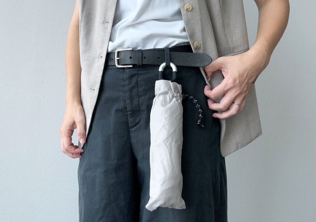 ベージュの折りたたみ傘が男性のベルトに吊り下げられている様子 ベージュの折りたたみ傘が男性のベルトに吊り下げられている様子