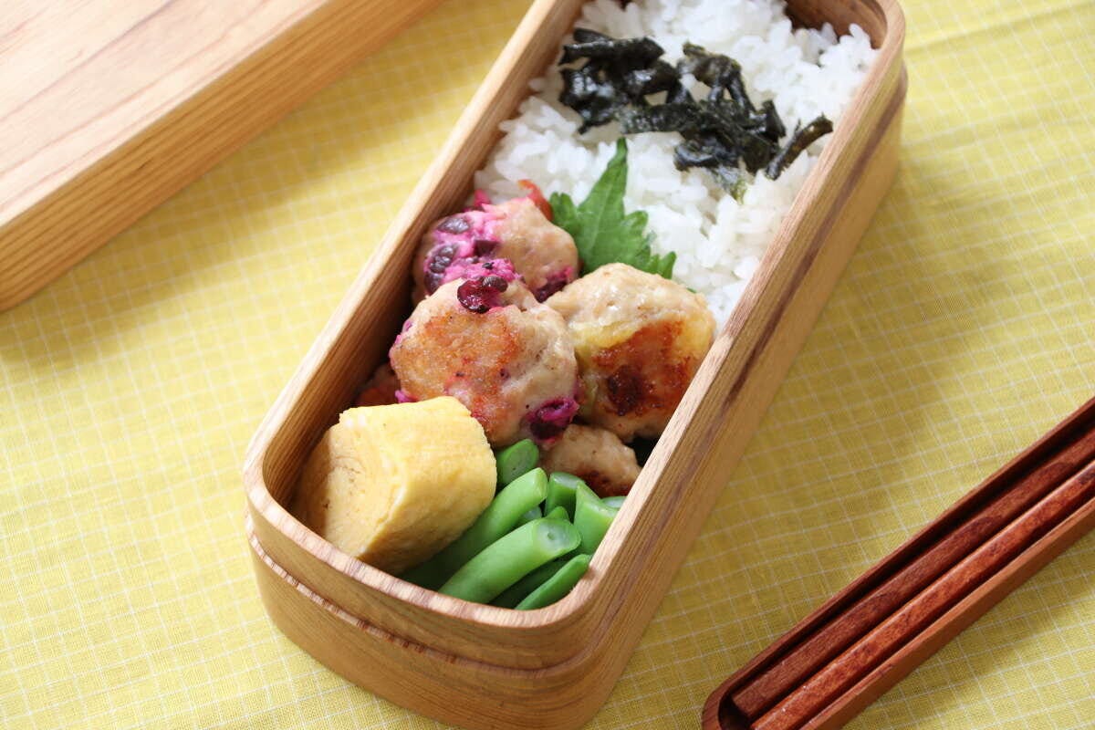 木製のお弁当箱に、ご飯、鶏つくね、卵焼き、いんげんが彩りよく詰められている