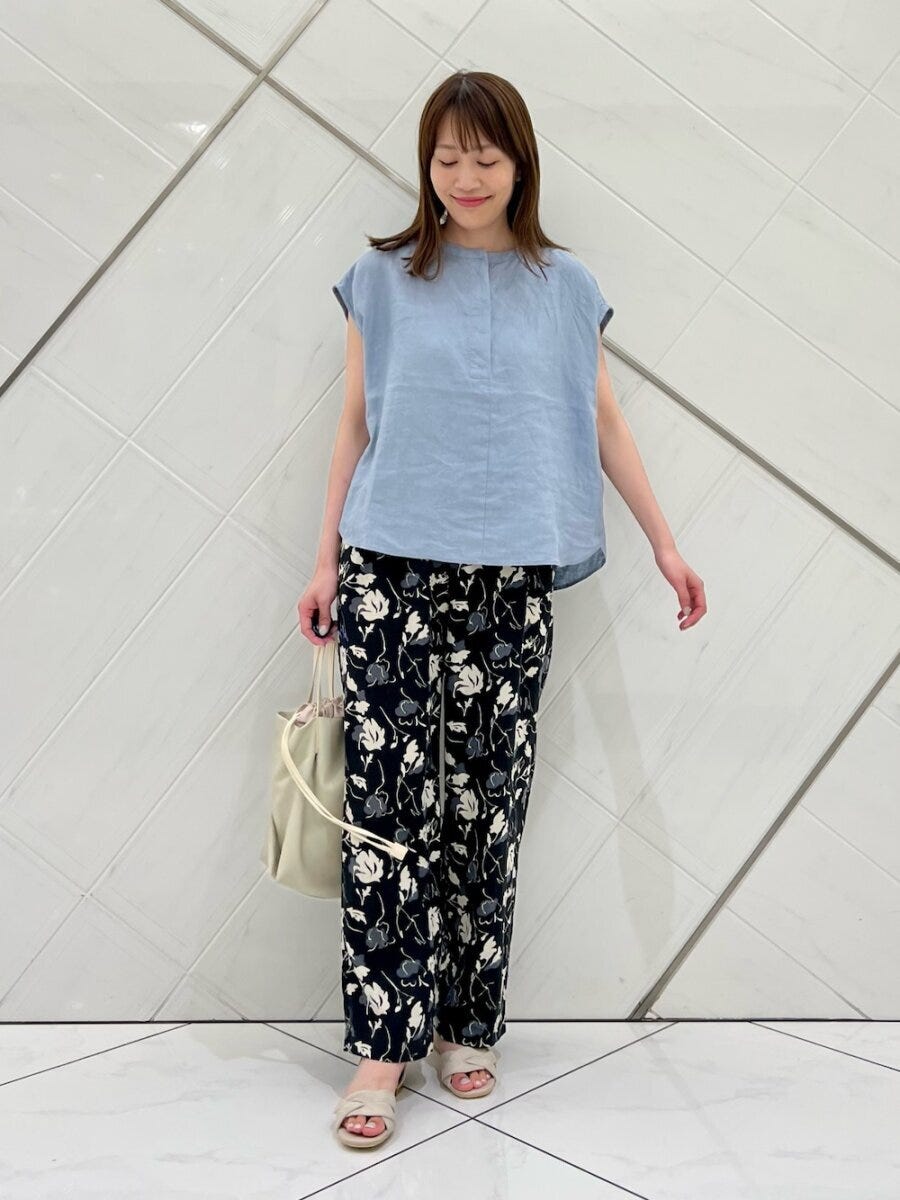 水色ブラウスと花柄パンツの女性が白いトートバッグを持つ