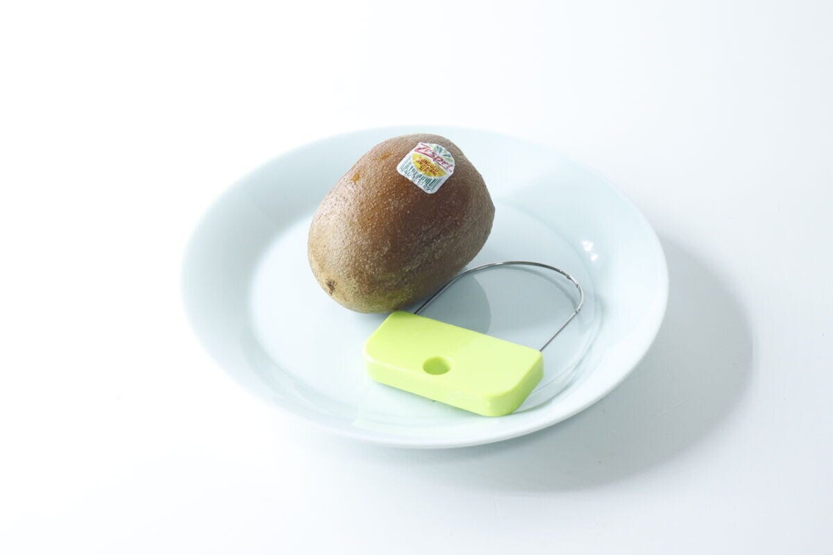 白い皿にキウイと緑色の皮むき器が置かれている