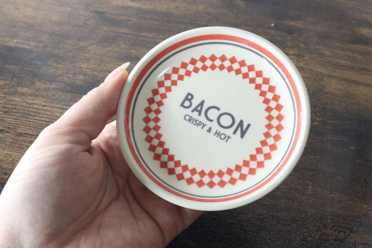 赤いチェック柄とBACONのロゴが入ったMサイズのプレートを手に持っている様子 赤いチェック柄とBACONのロゴが入ったMサイズのプレートを手に持っている様子