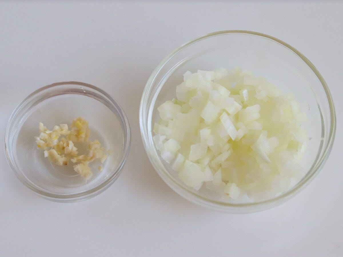 みじん切りのにんにくと粗みじん切りのたまねぎをそれぞれガラスボウルに入れた下準備の俯瞰写真