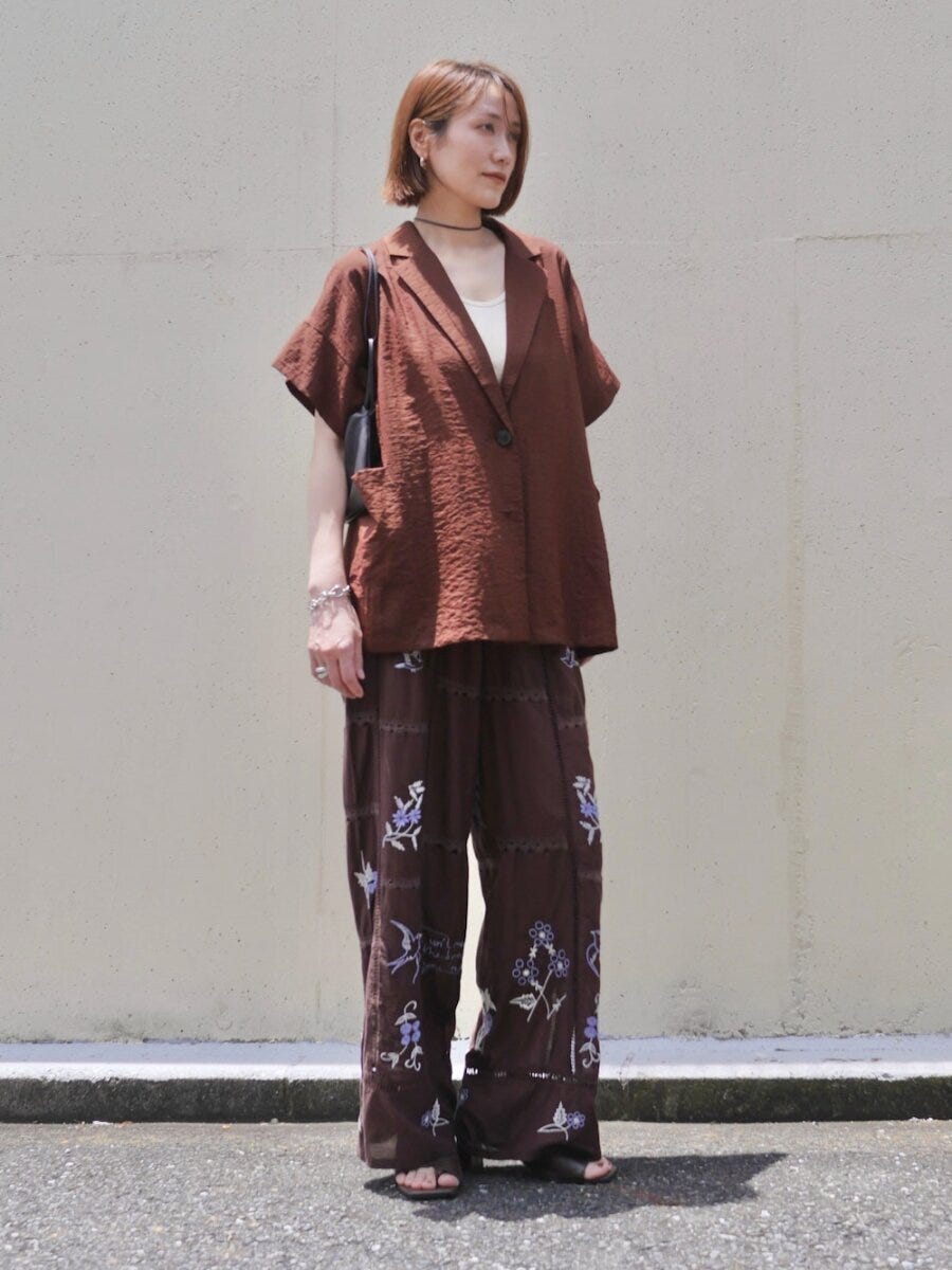 茶色の半袖ジャケットと刺繍柄パンツの女性