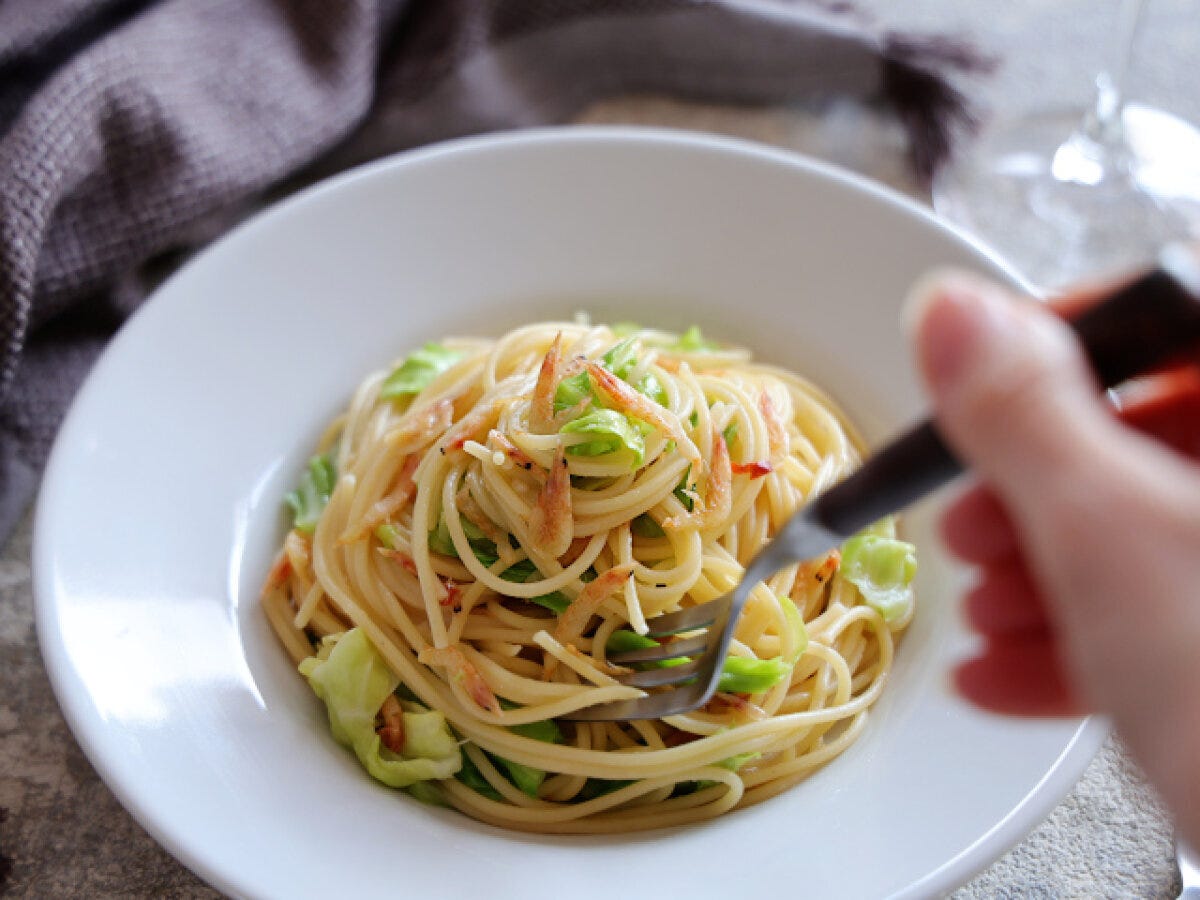 白い皿に盛られた春キャベツと桜海老のスパゲッティをフォークでつまもうとしている完成品写真