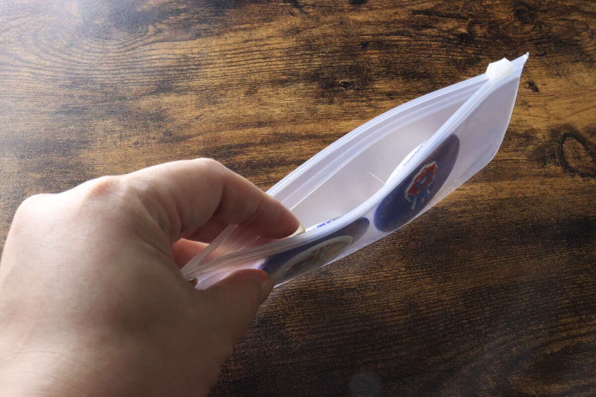 ジッパーを開けてマチのないポーチの内部に丸い缶バッジを入れている手元 ジッパーを開けてマチのないポーチの内部に丸い缶バッジを入れている手元