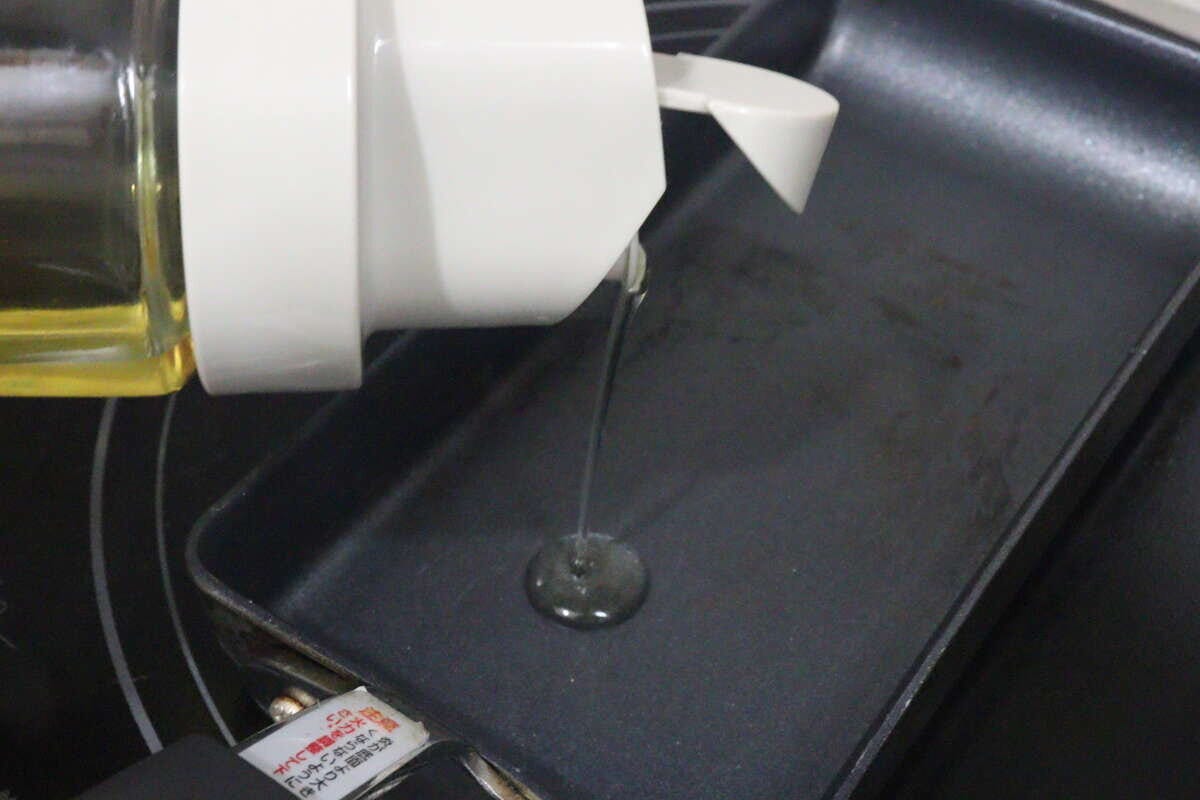 オイルボトルからフライパンに食用油を注いでいる様子 オイルボトルからフライパンに食用油を注いでいる様子
