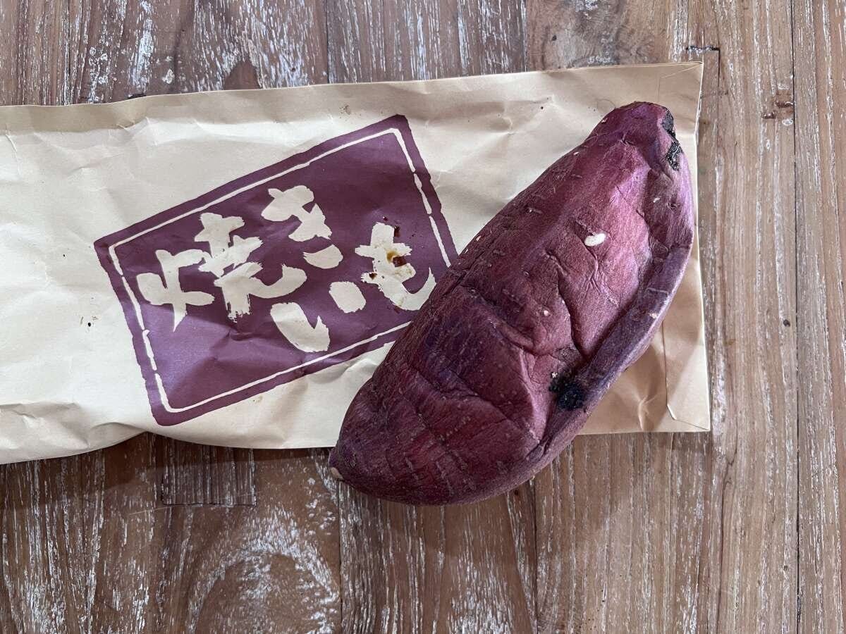 茶色い紙袋に入った焼き芋が木目のテーブルに置かれている 茶色い紙袋に入った焼き芋が木目のテーブルに置かれている