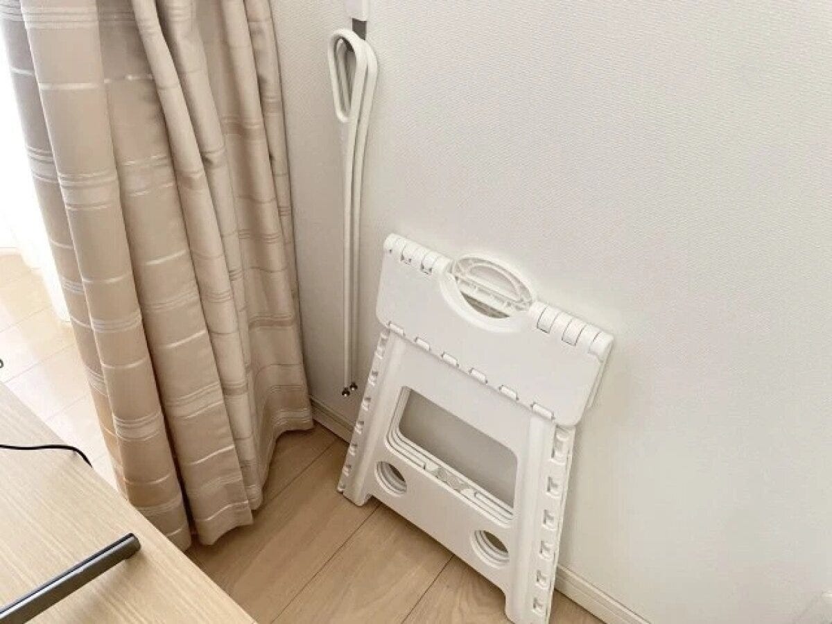 テレビボードの背面に折り畳み式のステップ台と掃除用具を立てかけている様子