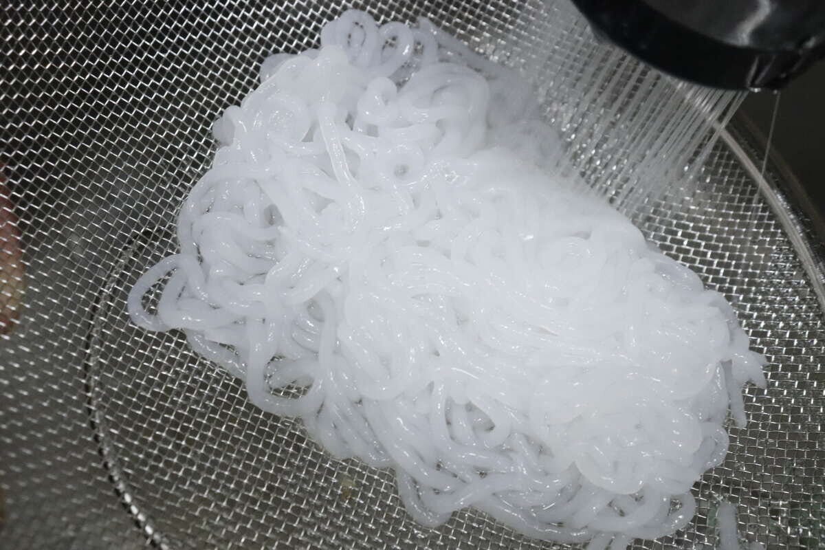 ザルに入ったこんにゃくヌードルを水で洗っている様子 ザルに入ったこんにゃくヌードルを水で洗っている様子