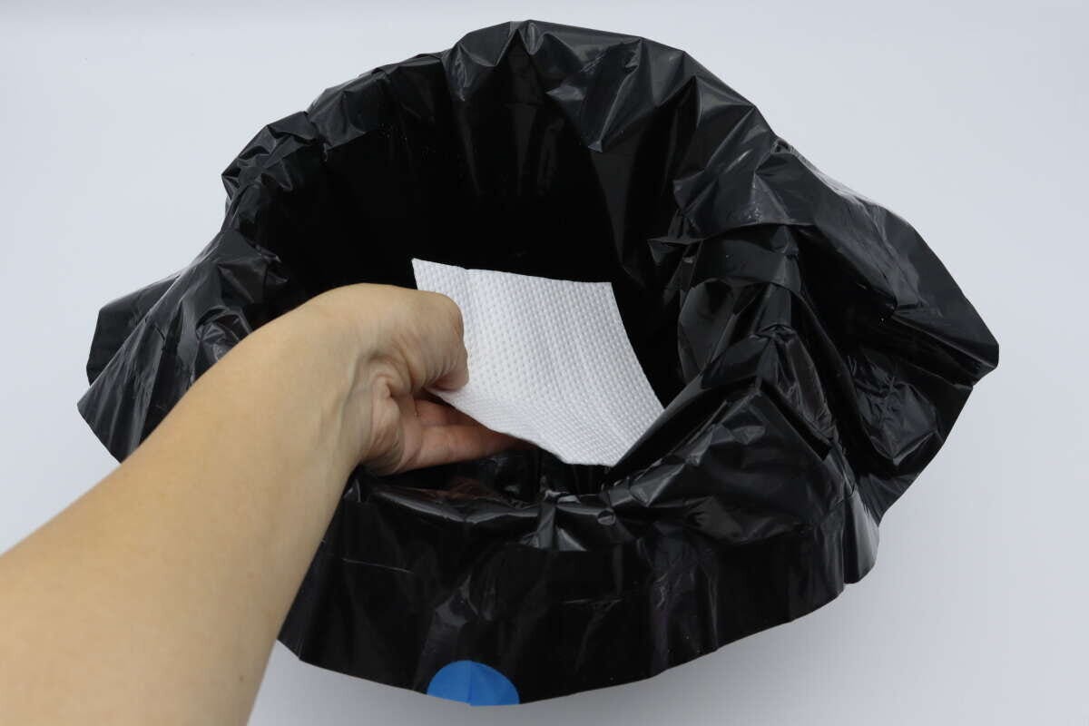 黒いビニール袋を被せたゴミ箱に吸水シートを入れる手
