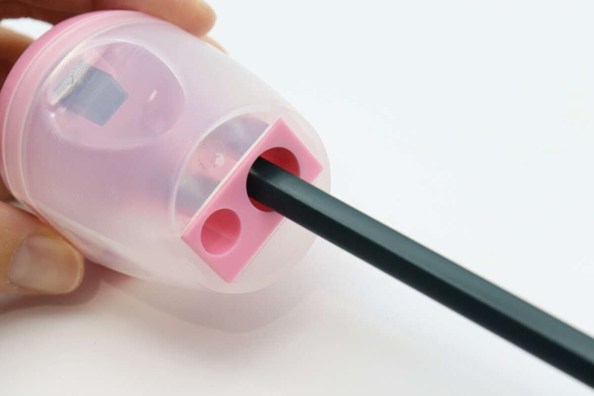 黒い鉛筆をゴミ箱型鉛筆削りの穴に差し込んでいる手元 黒い鉛筆をゴミ箱型鉛筆削りの穴に差し込んでいる手元
