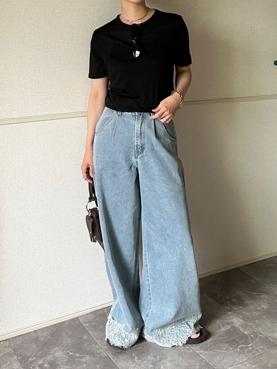 黒いシアーTシャツとデニムパンツを着用した女性がサングラスを胸元にかけバッグを持って立っている