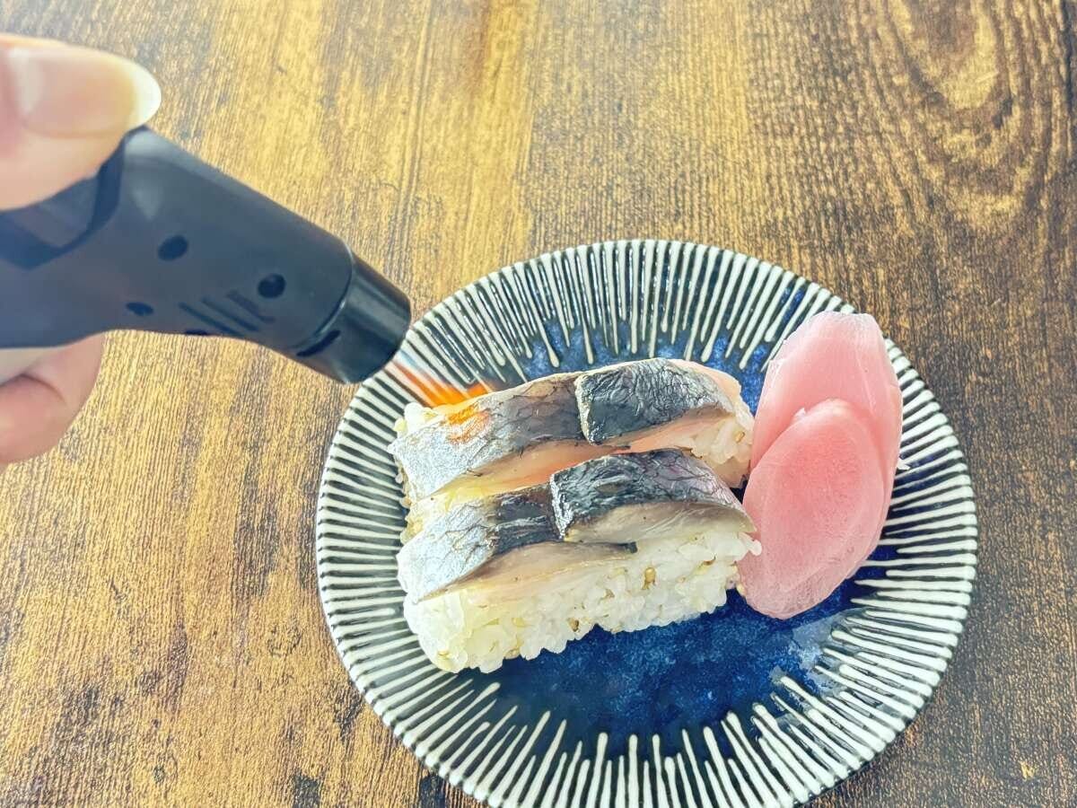 手がダイソーのガスバーナーを使いお皿に乗った鯖寿司を炙っている 手がダイソーのガスバーナーを使いお皿に乗った鯖寿司を炙っている