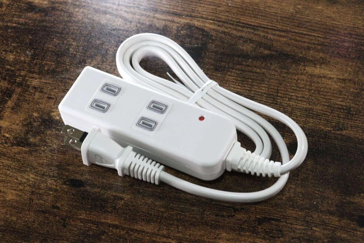 白い3個口の電源タップが木製のテーブルに置かれ、コードは束ねられている