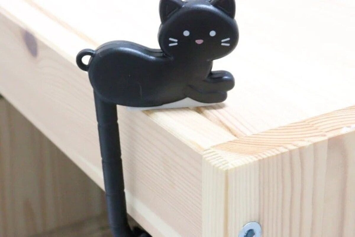 黒猫のバッグフックを木製テーブルの端に引っ掛けている 黒猫のバッグフックを木製テーブルの端に引っ掛けている