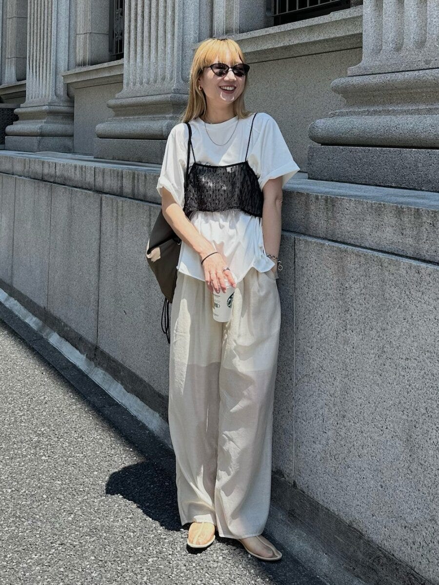 白Tとベージュパンツに黒ビスチェを重ね着しコーヒーを持つ女性