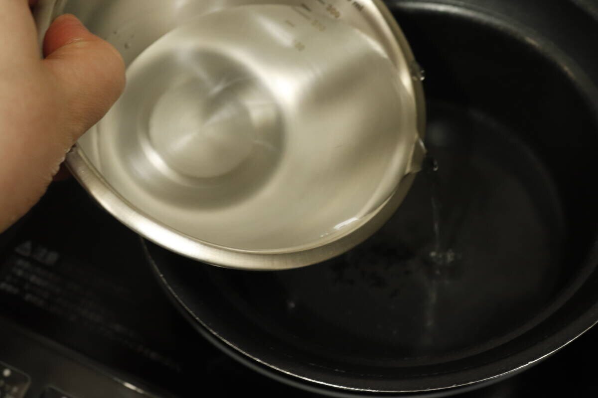 目盛り付きボウルで水を鍋に注ぎ入れる手元