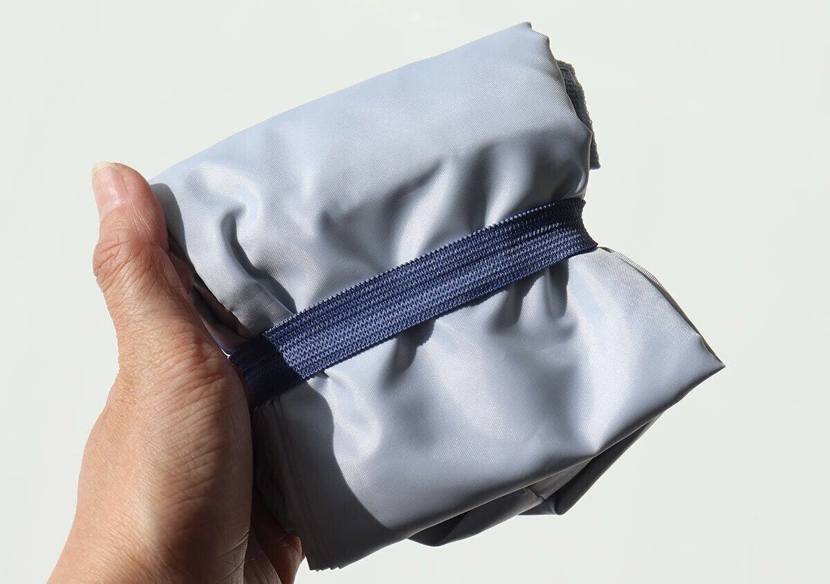 コールマンのライトブルートートバッグをゴムバンドで小さくまとめた状態を片手で持っているコンパクト収納写真 コールマンのライトブルートートバッグをゴムバンドで小さくまとめた状態を片手で持っているコンパクト収納写真