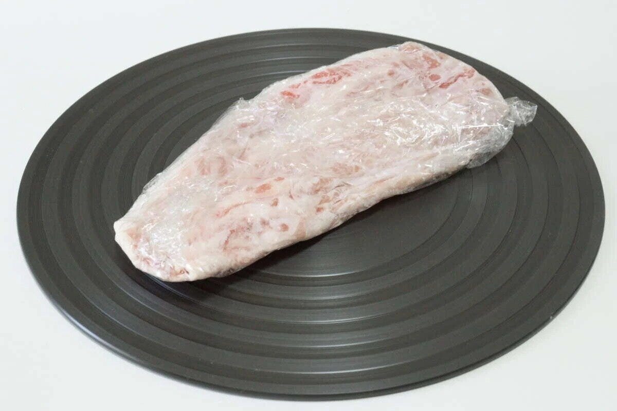 黒い円形の解凍プレートにラップされた冷凍肉が乗っている 黒い円形の解凍プレートにラップされた冷凍肉が乗っている