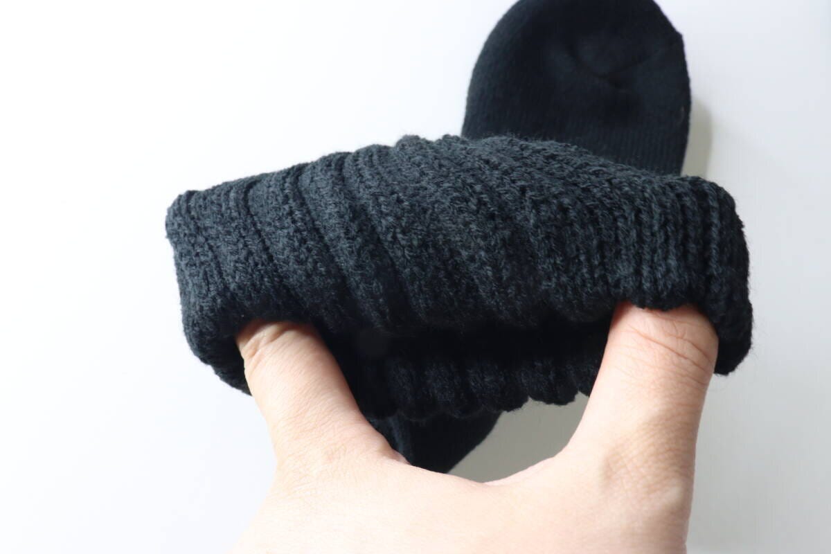 手で黒い靴下の履き口を広げ、ゆったりとした伸縮性を確認している様子。