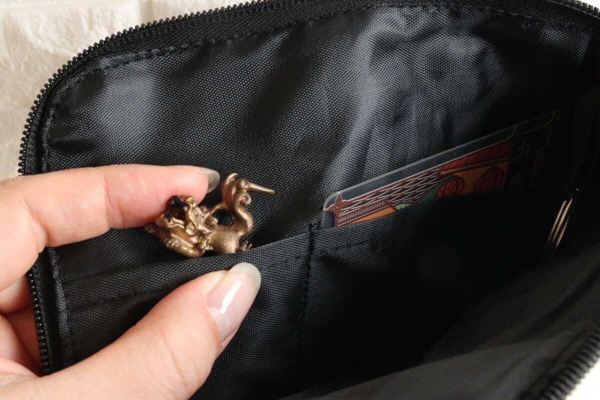 黒いポーチの内ポケットにICカードと小さな金属製の飾りが収納されている様子