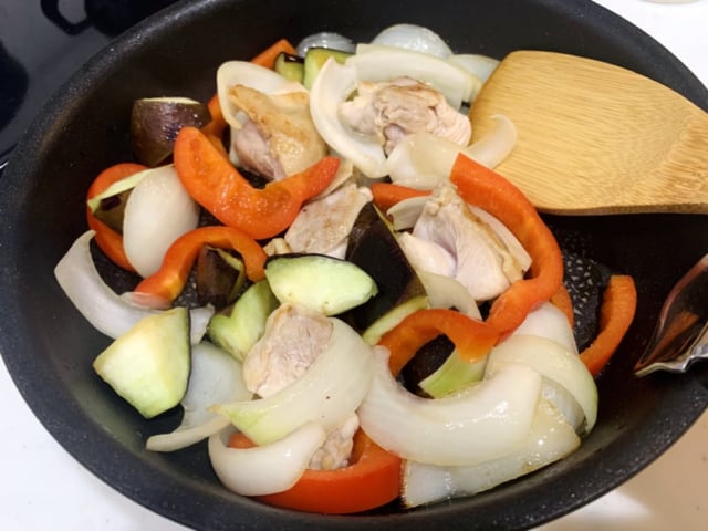 食材（なす・パプリカ・玉ねぎ・鶏モモ肉）をフライパンで炒めている様子