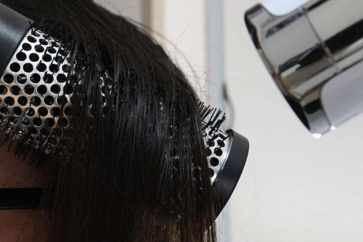 女性の髪にロールヘアブラシを当て、ドライヤーでブローしている様子