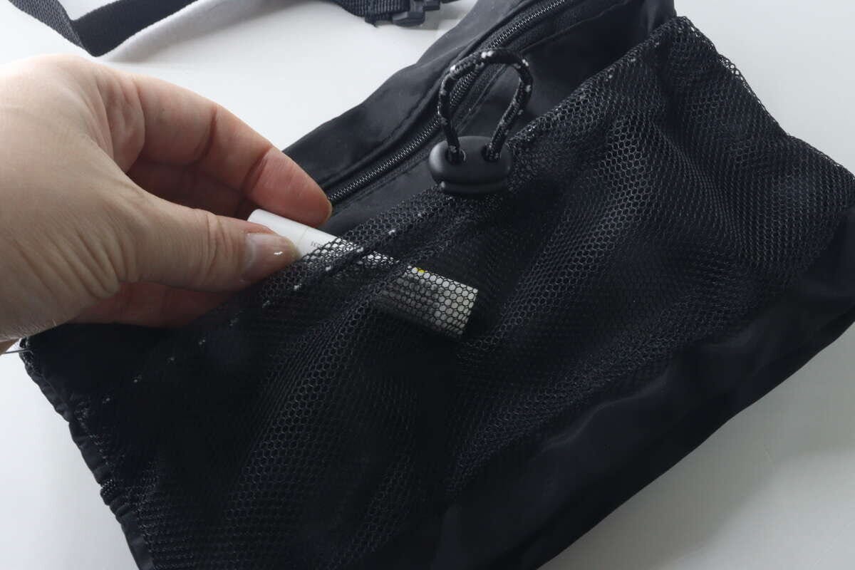 手が黒いショルダーバッグのメッシュポケットにリップクリームを入れている