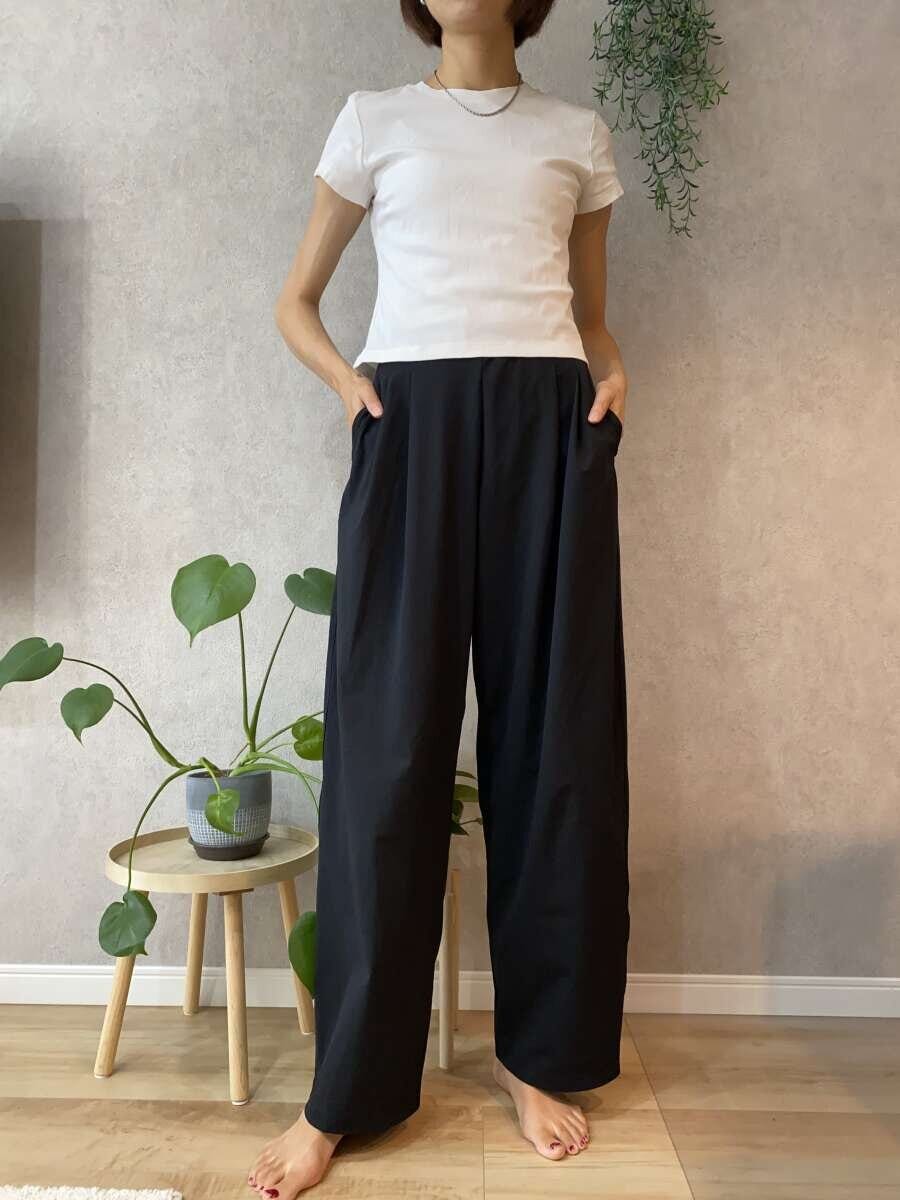 黒いワイドパンツと白いTシャツを着て立つ女性